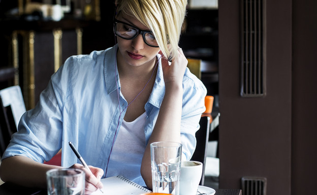 אישה יושבת וכותבת בבית קפה (אילוסטרציה: Shutterstock)