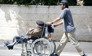 עובד פיליפיני מוביל זקן בכיסא גלגלים (צילום: אביר סולטן, פלאש 90)
