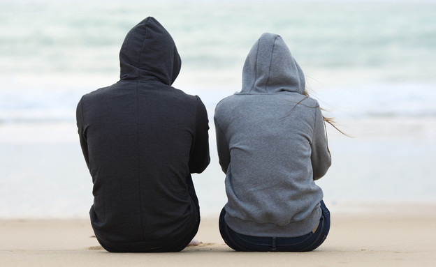 בחור ובחורה יושבים על החוף, ראשים מכוסים בקפוצ'וני (אילוסטרציה: ShutterStock)