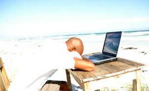 אדם יושב בים מול שולחן עם לפטופ (צילום: jupiter images)