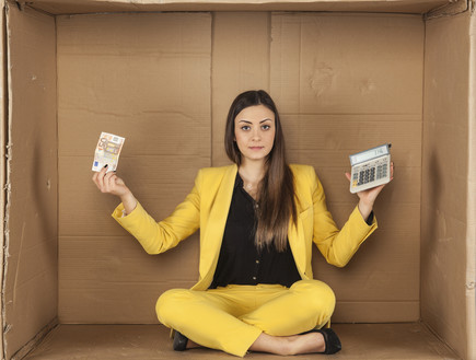 אשת עסקים יושבת בתוך קופסת קרטון עם מחשבון ושטר כסף (אילוסטרציה: Maslowski Marcin, Shutterstock)