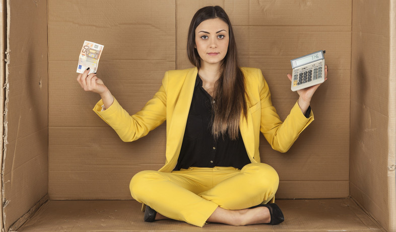 אשת עסקים יושבת בתוך קופסת קרטון עם מחשבון ושטר כסף (אילוסטרציה: Maslowski Marcin, Shutterstock)