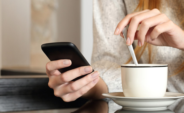 אישה שותה קפה ומסתכלת בטלפון הסלולרי (אילוסטרציה: Antonio Guillem, Shutterstock)