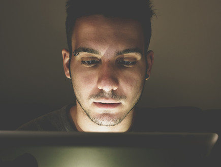 גבר צופה במחשב בחדר חשוך (צילום: ShutterStock)