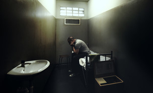 אסיר יושב בכלא (צילום: By Peppinuzzo, ShutterStock)