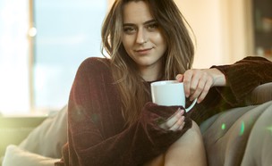 אישה מחייכת יושבת על ספה ושותה קפה (אילוסטרציה: rw studios, unsplash)
