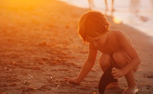 ילד משחק על החוף עם הוריו ברקע (צילום: monica gozalo, unsplash)
