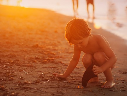 ילד משחק על החוף עם הוריו ברקע (צילום: monica gozalo, unsplash)