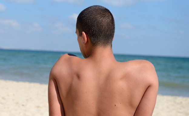נער יושב על החוף בגבו למצלמה (צילום: By Dafna A.meron, shutterstock)