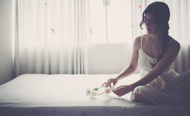 אישה יושבת על מיטה עם זר לבן (אילוסטרציה: unsplash)