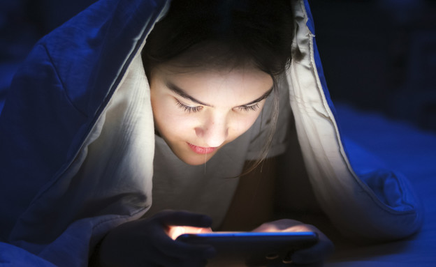 ילדה מתחת לשמיכה עם טלפון סלולרי (אילוסטרציה: By Dafna A.meron, shutterstock)
