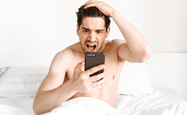 גבר במיטה עם טלפון (צילום: Dean Drobot, shutterstock)