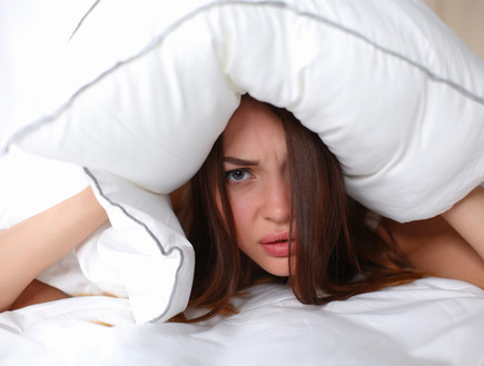 אישה שוכבת על מיטה ואוטמת אוזניים עם כרית (אילוסטרציה: lenetstan, shutterstock)