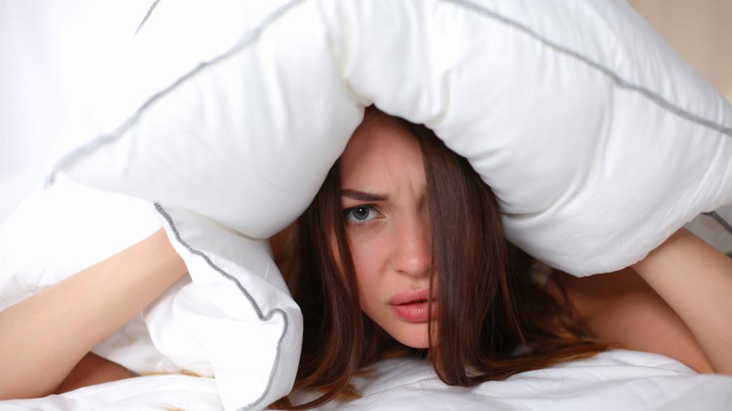 אישה שוכבת על מיטה ואוטמת אוזניים עם כרית (אילוסטרציה: lenetstan, shutterstock)
