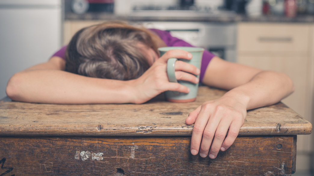 אישה עייפה מרוחה על השולחן עם כוס קפה ביד (צילום: LoloStock / Shutterstock)