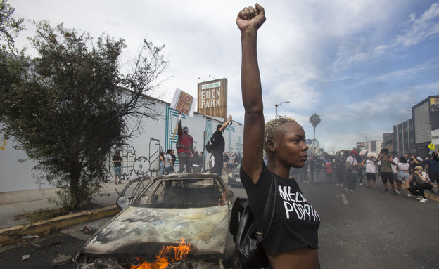 מפגינה על רקע מכונית שרופה במהומות בלוס אנג'לס (צילום: AP)