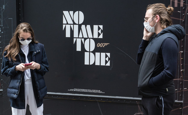 אנשים עם מסיכות פנים ליד כרזה לסרט של ג'יימס בונד בלונדון (צילום: rodwey2004, shutterstock)