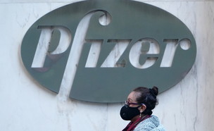 אישה עם מסכה חולפת ליד הבניין המרכזי של חברת פייזר (צילום: רויטרס)