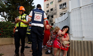 חובשים ישראלים עומדים ליד נשים שבניין מגוריהן נפגע מרקטה באשקלון (צילום: רויטרס)