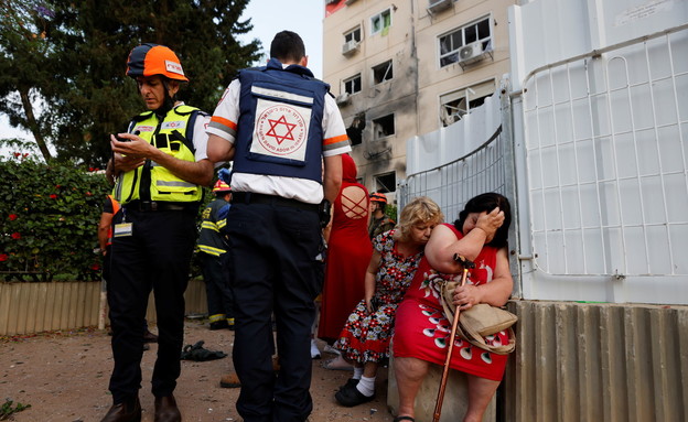 חובשים ישראלים עומדים ליד נשים שבניין מגוריהן נפגע מרקטה באשקלון (צילום: רויטרס)