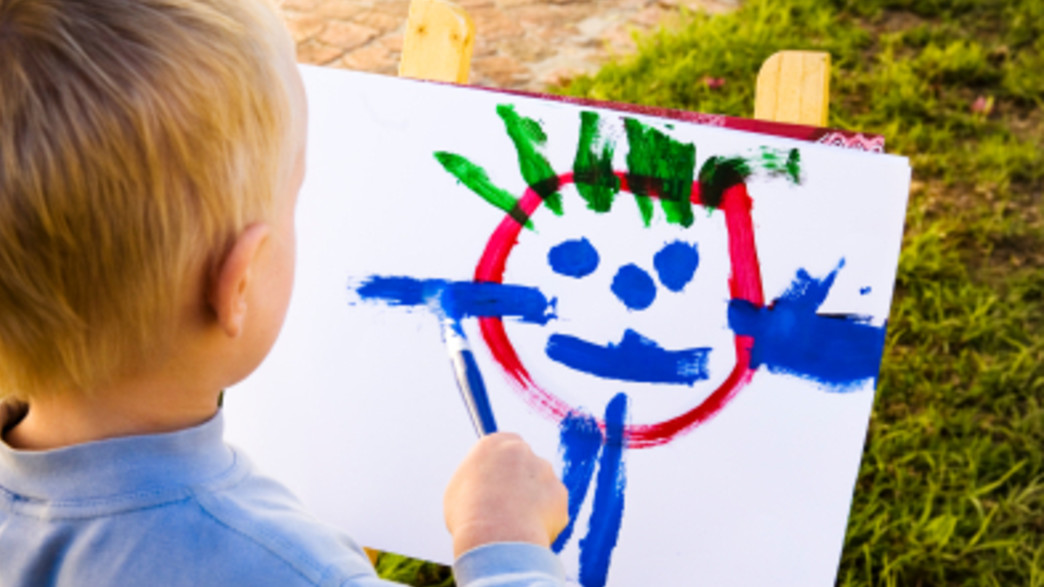 ילד מצייר ציור עם מכחול מצולם מגבו ילד מצייר ציור עם מכחול מצולם מגבו