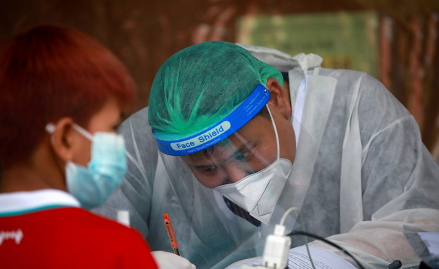 עובד מערכת הבריאות בתאילנד רושם ילד שאובחן חיובי לקורונה (צילום: רויטרס)