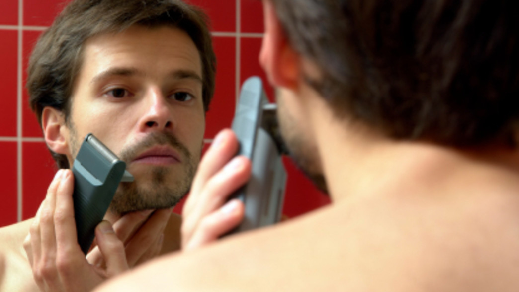 גבר מתגלח במכונה מול מראה גבר מתגלח במכונה מול מראה