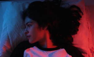 אישה שוכבת על מיטה בחולצה ורודה (אילוסטרציה: Sam Rios, unsplash)