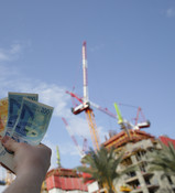 יד מחזיקה שטרות מול אתר בנייה