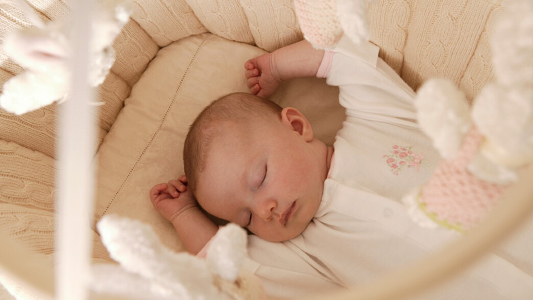 תינוק ישן בידיים בעריסה מעליו מובייל ארנבים