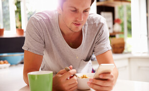 גבר אוכל ארוחת בוקר ומסתכל בטלפון סלולרי (צילום: By Dafna A.meron)