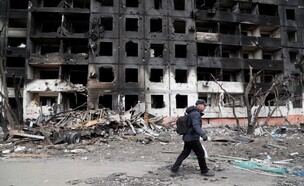 אדם הולך ליד בניין שנהרס בהפגזות בעיר מריופול (צילום: חדשות 12)