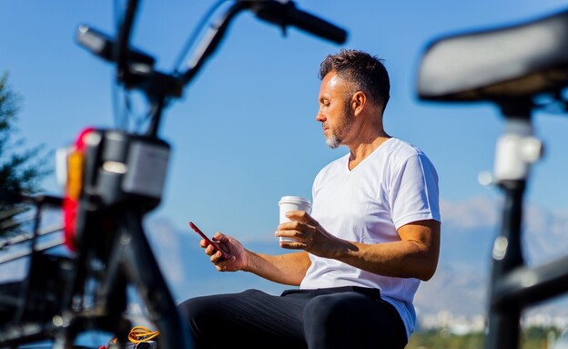 גבר עם טלפןו ליד אופניים (צילום: Shutterstock)