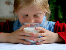 ילדה באדום וכחול יושבת ומחזיקה כוס חלב ומביטה בו (צילום: Hallgerd, Istock)
