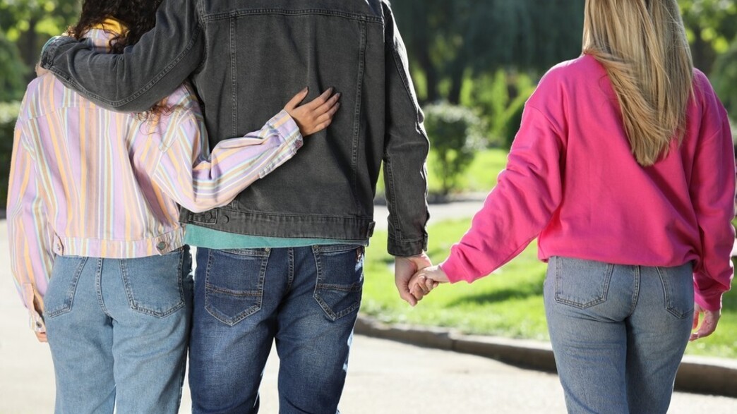 גבר מחזיק ידיים עם אישה אחרת בזמן שהוא מחבק את חברתו