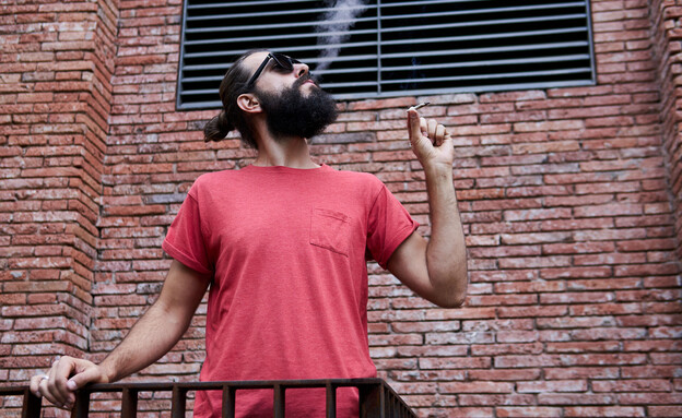איש מעשן קנאביס במרפסת (צילום: Aleksandra Belinskaya, shutterstock)