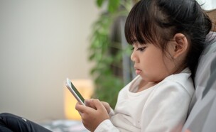 ילדה אסיאתית משחקת בסמארטפון (צילום: FAMILY STOCK/SHUTTERSTOCK)