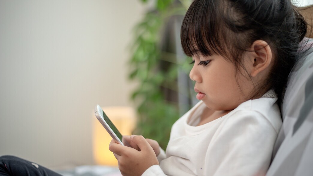 ילדה אסיאתית משחקת בסמארטפון (צילום: FAMILY STOCK/SHUTTERSTOCK)