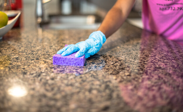 אישה מנקה משטח שיש במטבח עם ספוג (צילום: Nicole Glass Photography, SHUTTERSTOCK)