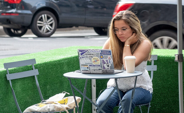 אישה יושבת בבית קפה מול מחשב נייד (צילום: Alexi Rosenfeld, Getty images)