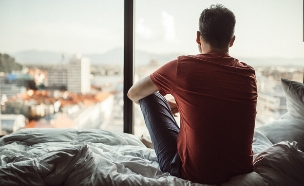 גבר יושב על מיטה ומסתכל על החלון (אילוסטרציה: South_agency)