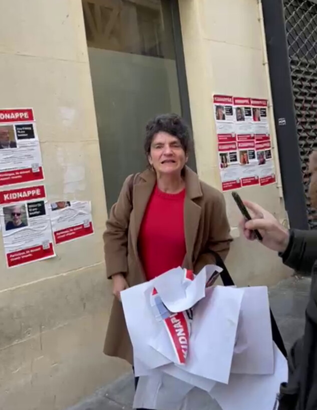 אישה צרפתייה תולשת את מודעות החטופים בצרפת, צילון (צילום: נועה זדה)