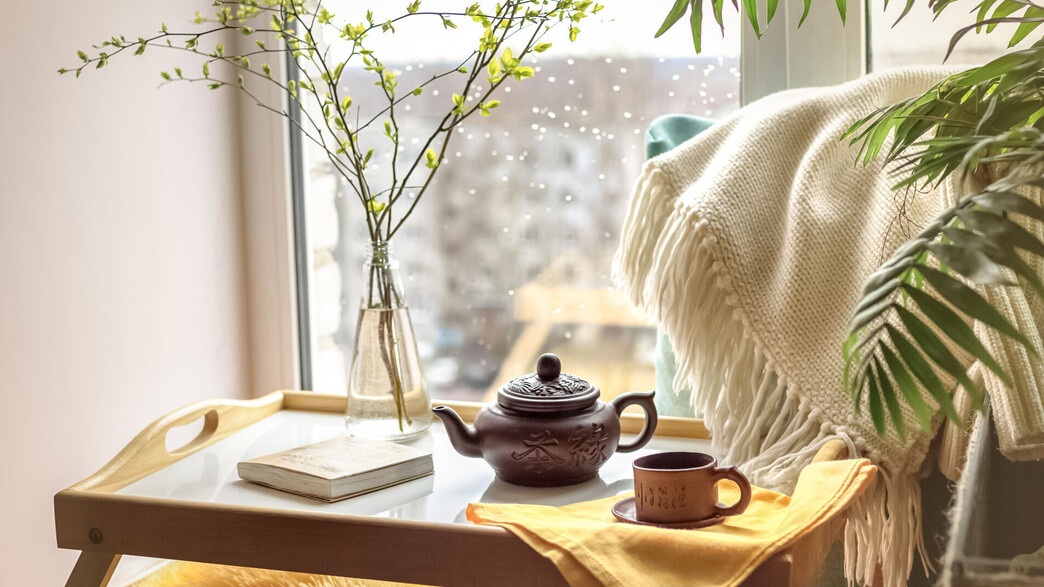 מגש עם קנקן תה ופרחים על אדן חלון כשבחוץ גשם (צילום: Olga Smolyak, SHUTTERSTOCK)