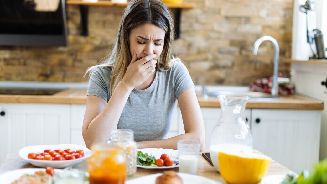 אישה מחזיקה את הבטן ליד שולחן האוכל אישה מחזיקה את הבטן ליד שולחן האוכל