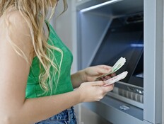 אישה בלונדינית מחזיקה שטרות ליד כספומט