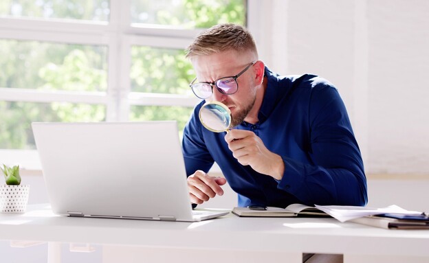 אדם במשרד עם זכוכית מגדלת על מחשב נייד (צילום: Andrey_Popov, shutterstock)