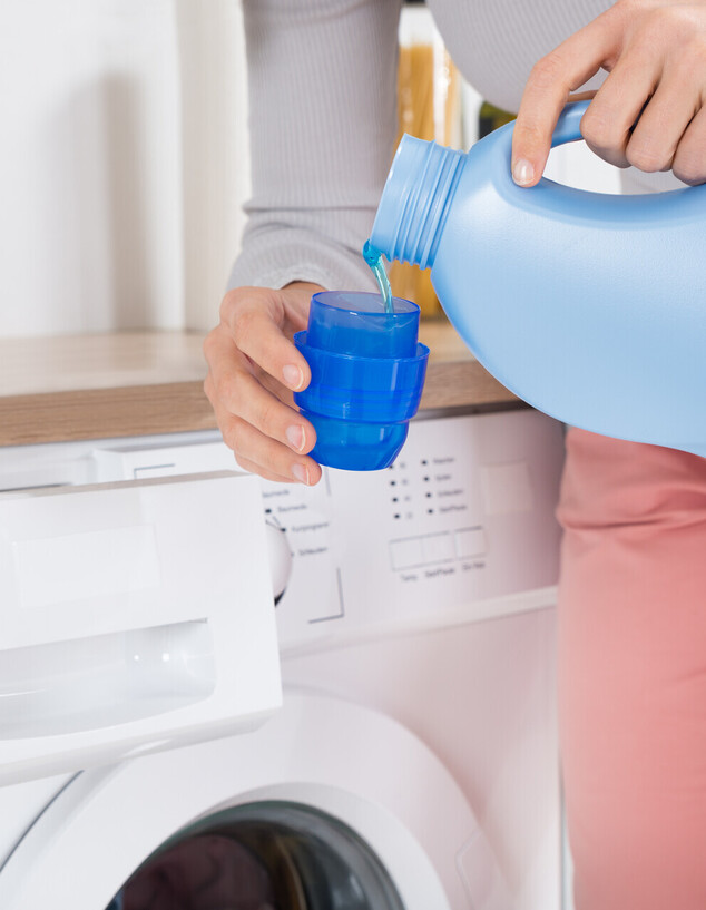 אישה שופכת נוזל כביסה מבקבוק לפקק, מכונת כביסה