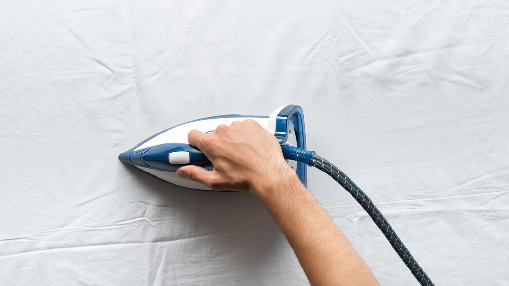 גיהוץ, יד עם מגהץ על בד לבן גיהוץ, יד עם מגהץ על בד לבן