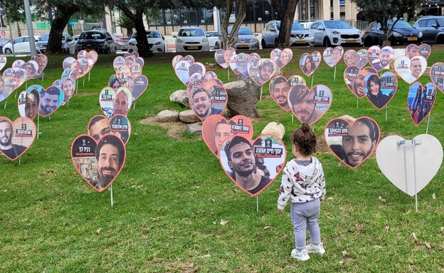 תמונות חטופים בגינה ברעננה וילדה קטנה צופה בהן (צילום: עומר בן נעים)