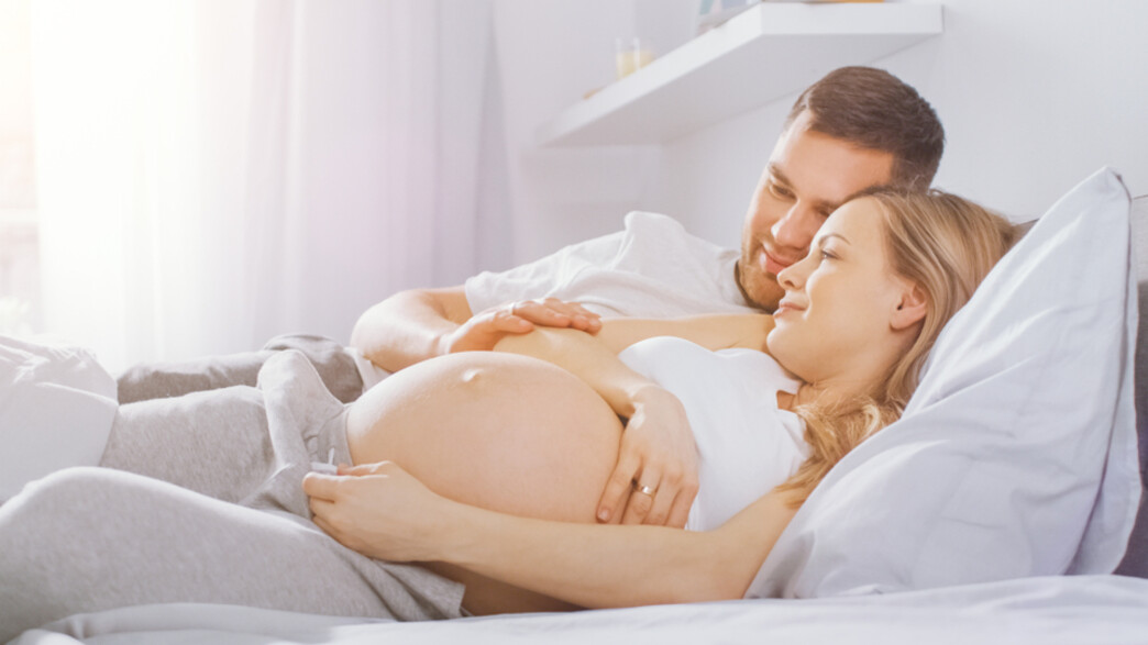 אישה בהיריון עם בן זוגה במיטה